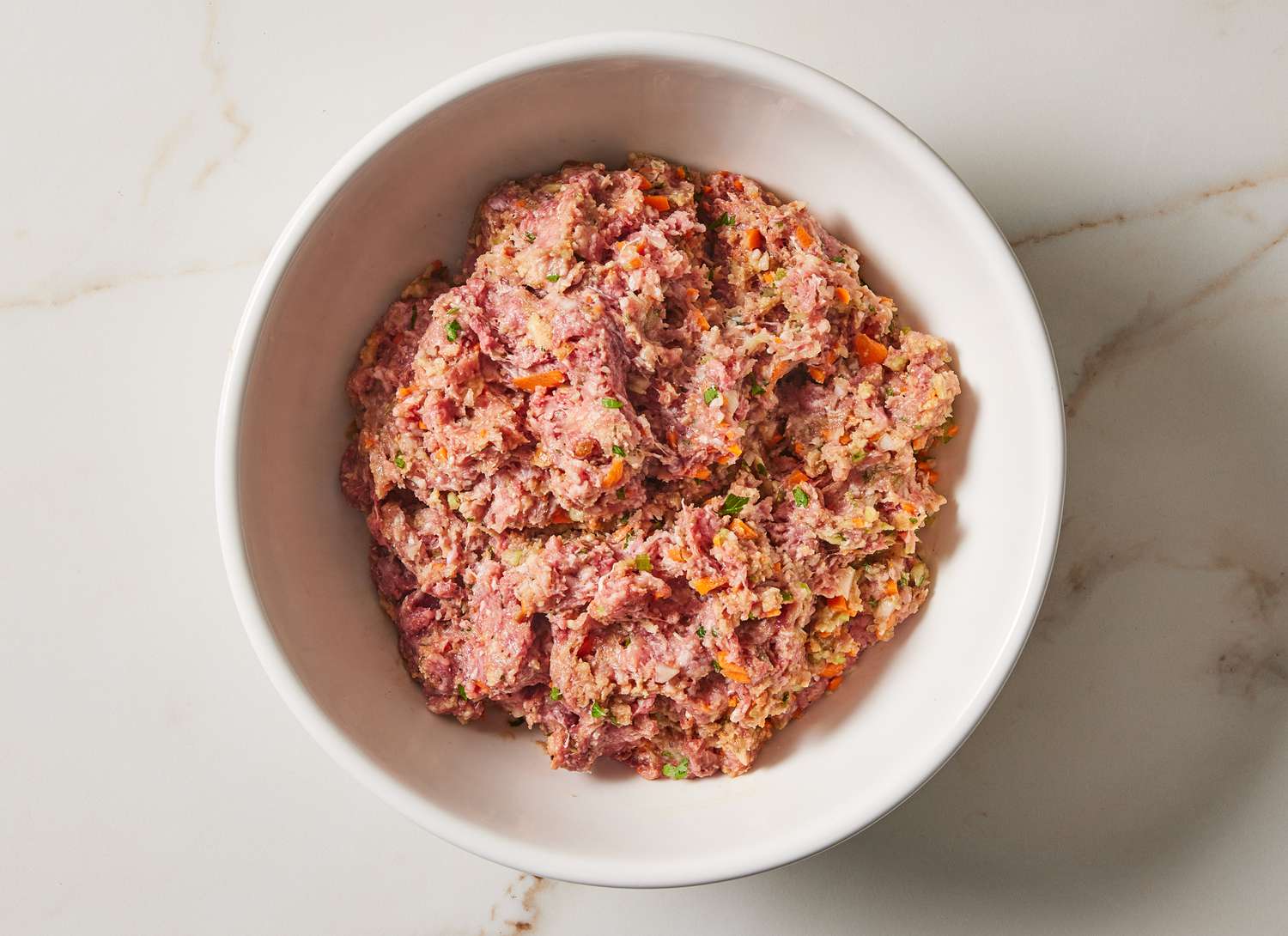 raw ground meat, vegetables and spices in a white bowl mixed together