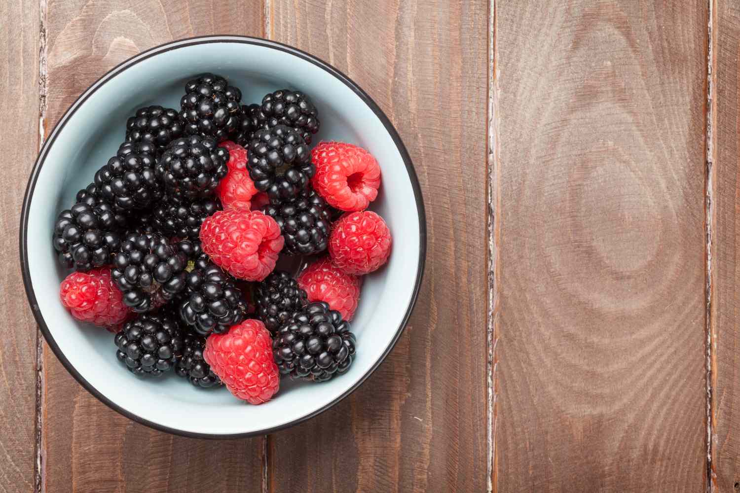 blackberries and raspberries in a white bowl on a wooden table