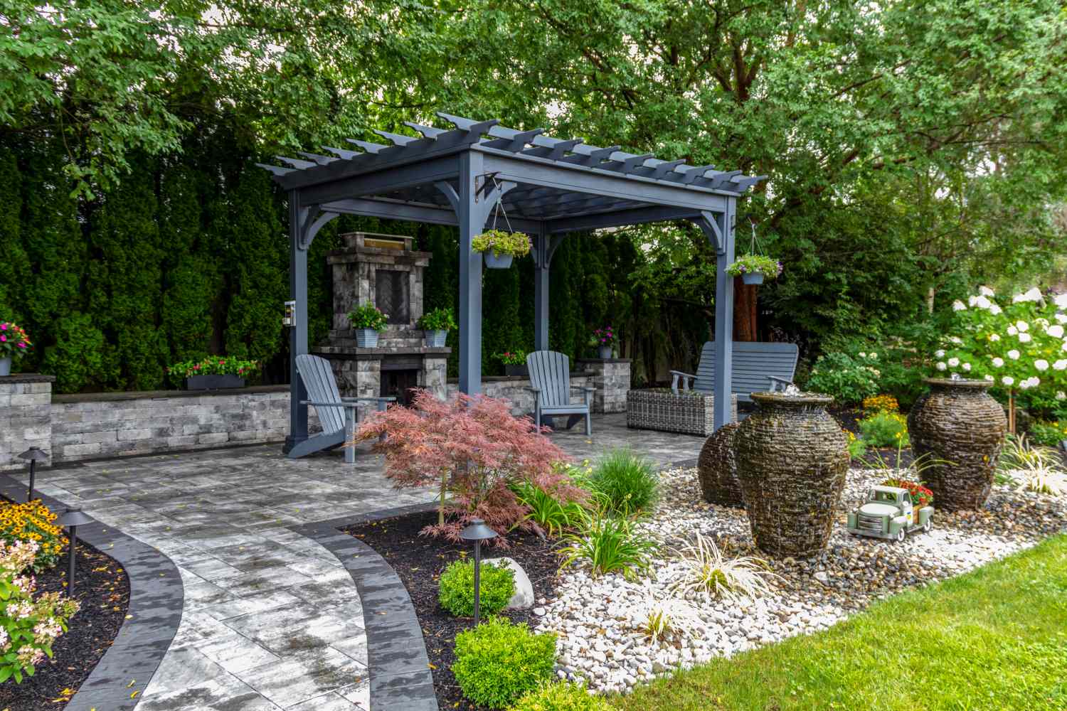 Outdoor seating area with a pergola, surrounded by landscaping and decorative stone features