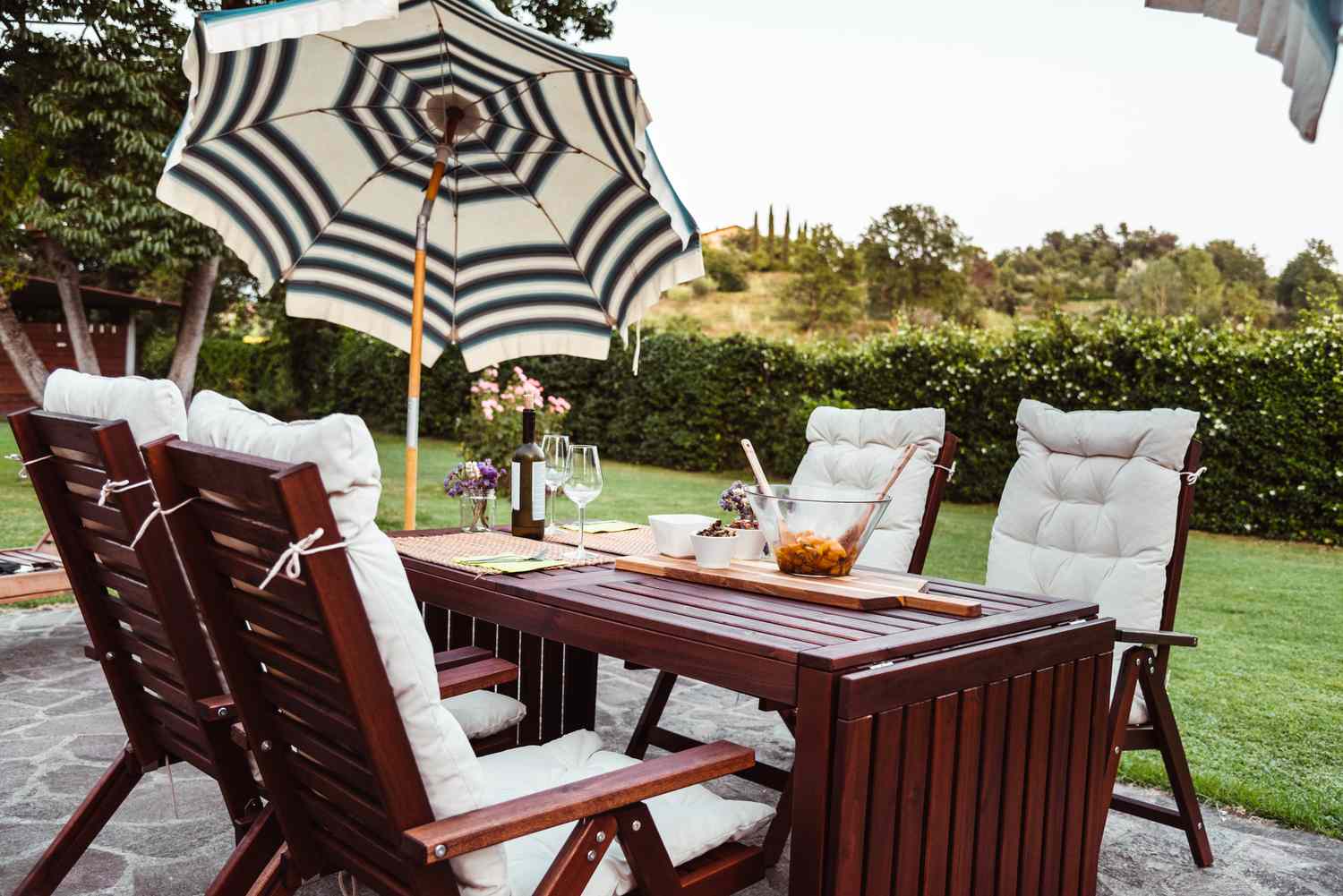 Outdoor patio set with a table chairs and an umbrella on a paved area in a garden setting