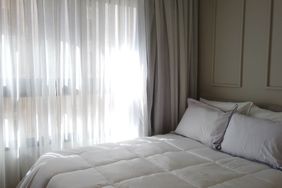 A bedroom with a neatly made bed and sheer curtains covering a window