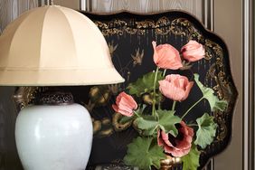 A table lamp a vase with flowers a decorative tray and small objects placed on a wooden surface