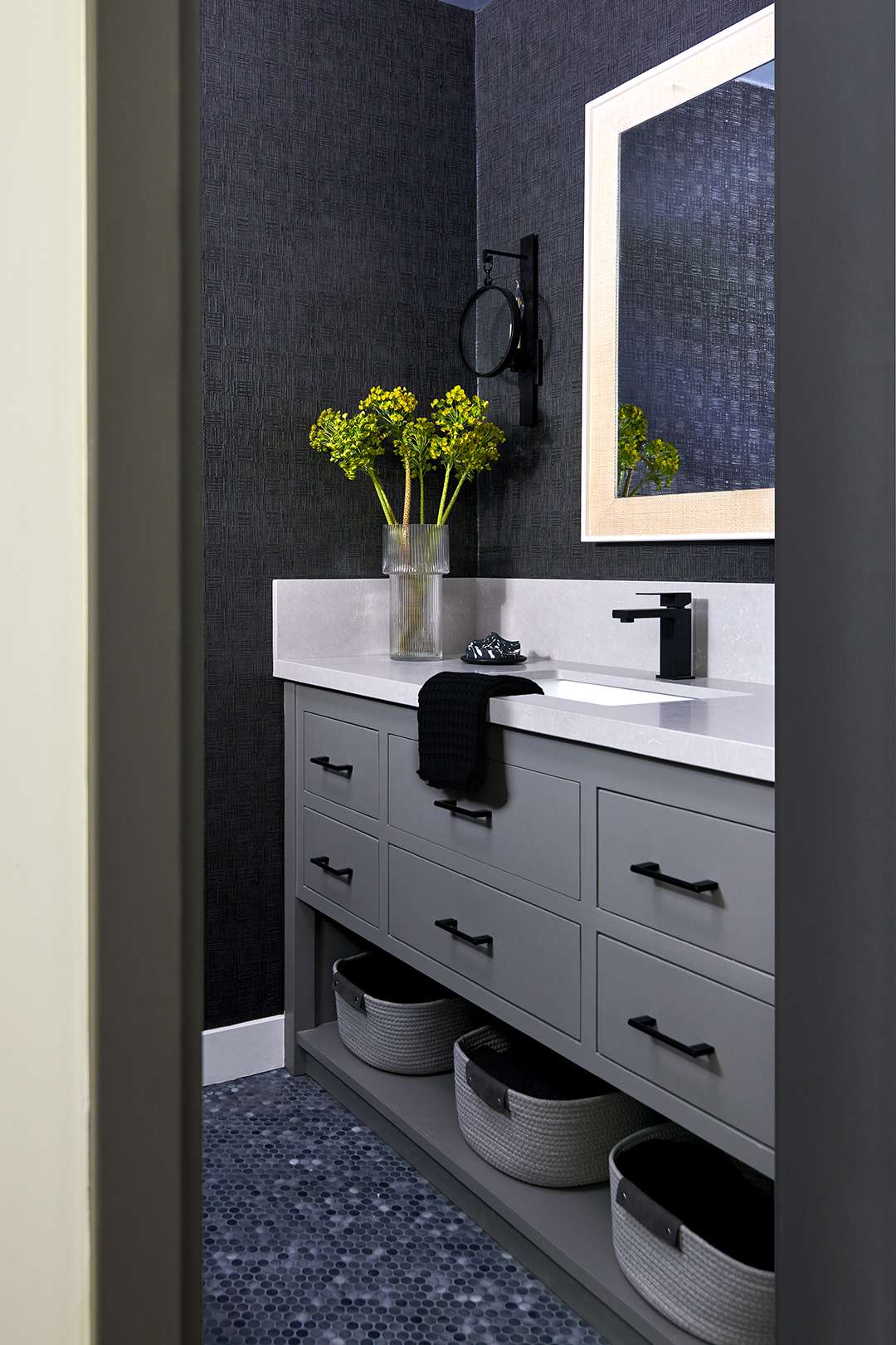 Modern bathroom interior with a gray vanity a rectangular mirror storage baskets and a jar with green foliage
