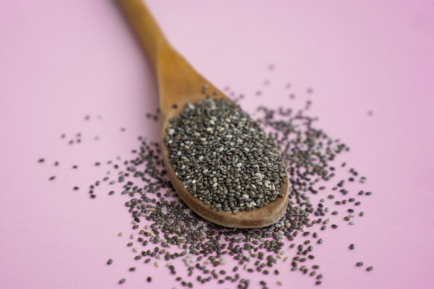 chia seeds in a wooden spoon and scattered on a pink-surface
