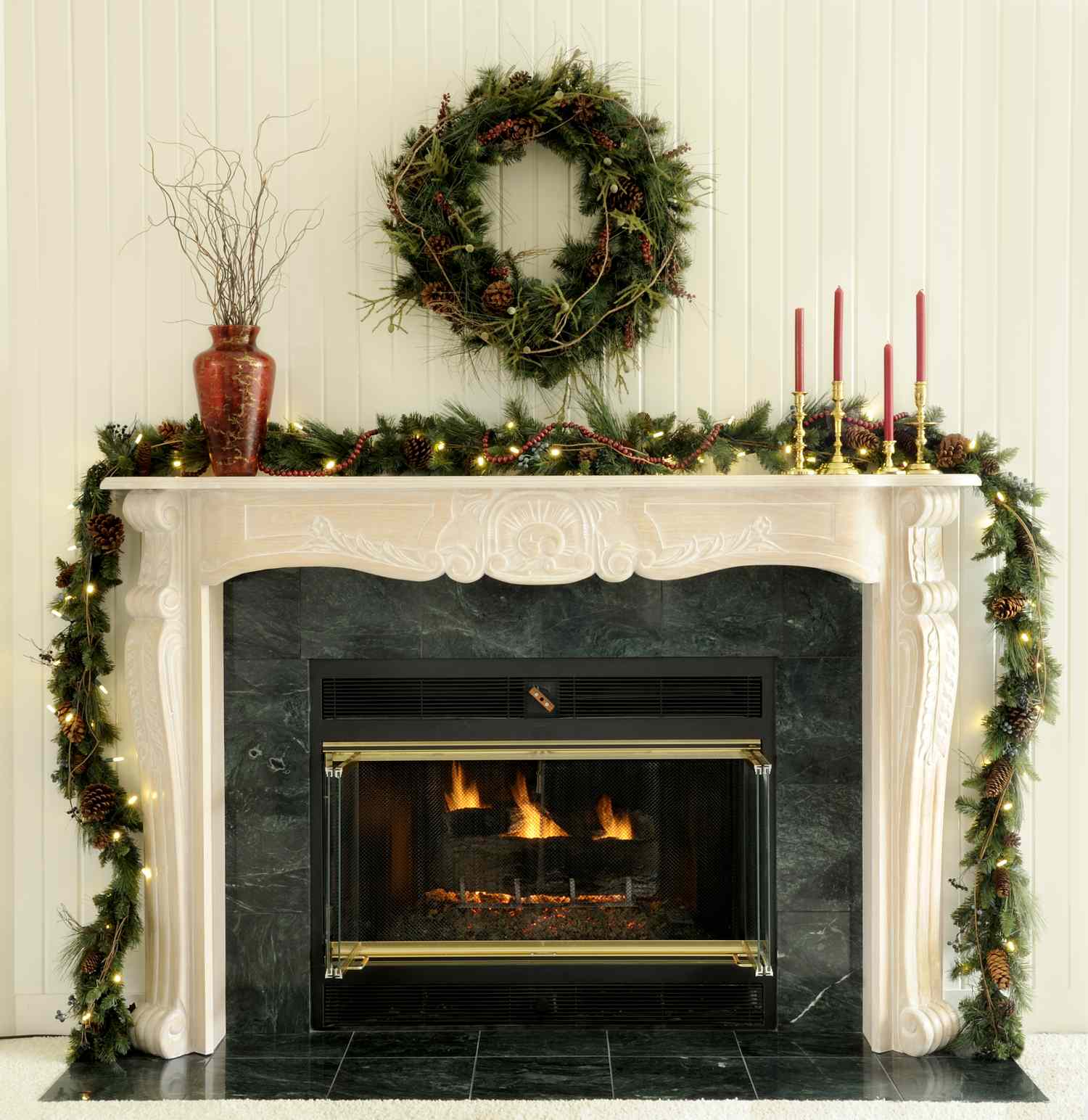 A fireplace decorated for the holidays with a wreath garland and candlesticks