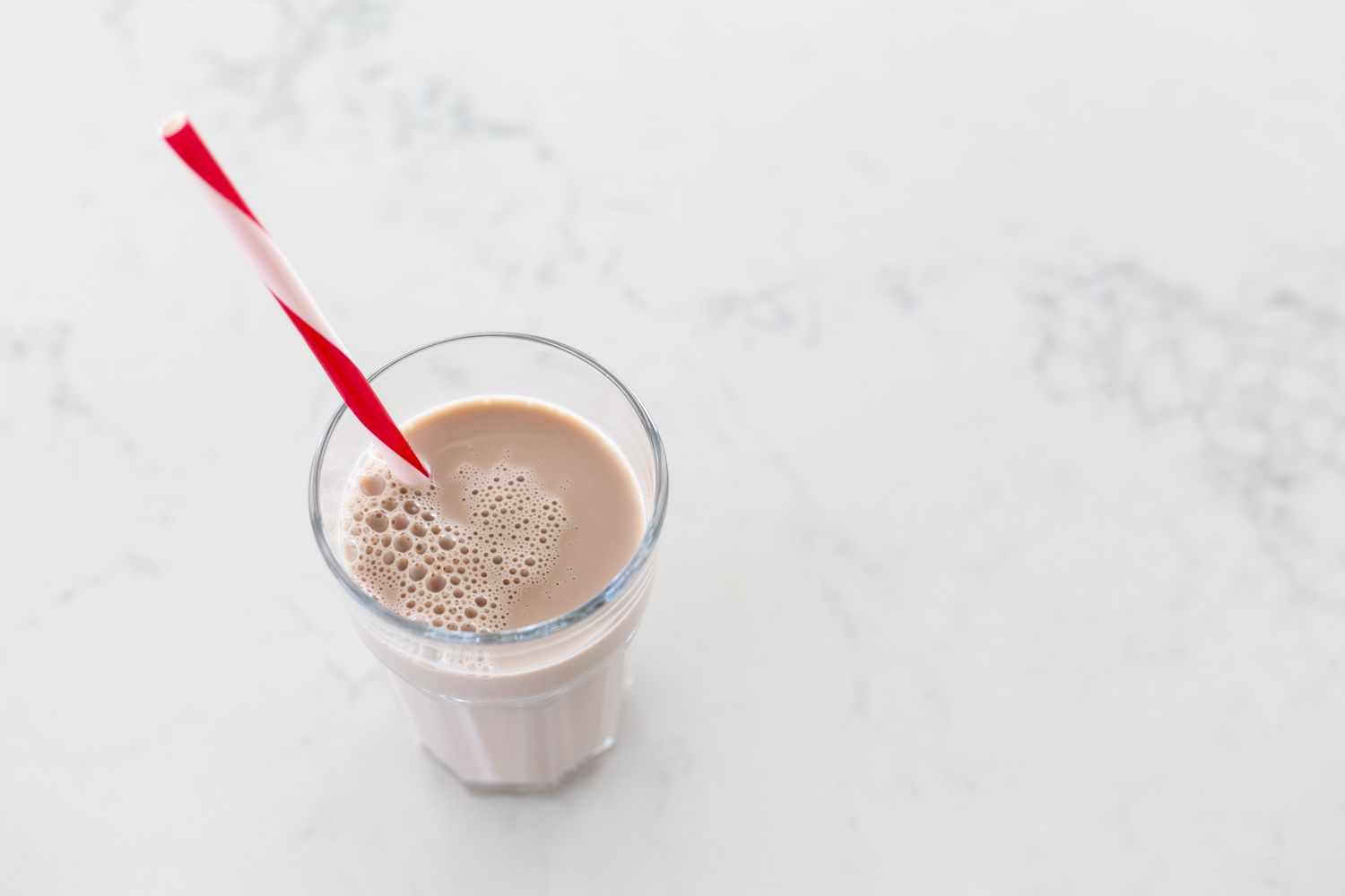 A glass of chocolate milk with a red and white striped straw on a marble surface