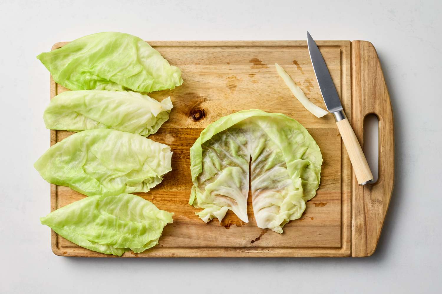 Cabbage leaves and a knife on a wooden cutting board possibly for preparation of stuffed cabbage
