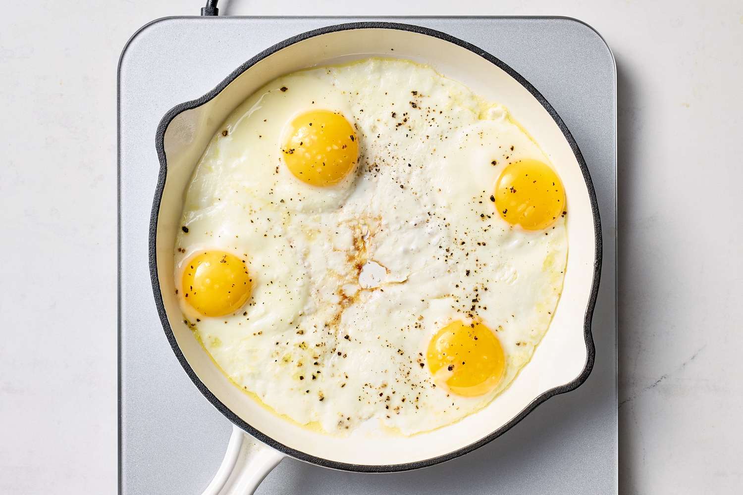 Four fried eggs in a skillet on a stovetop