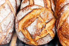 A loaf of sourdough bread with a rustic crust sitting alongside other loaves
