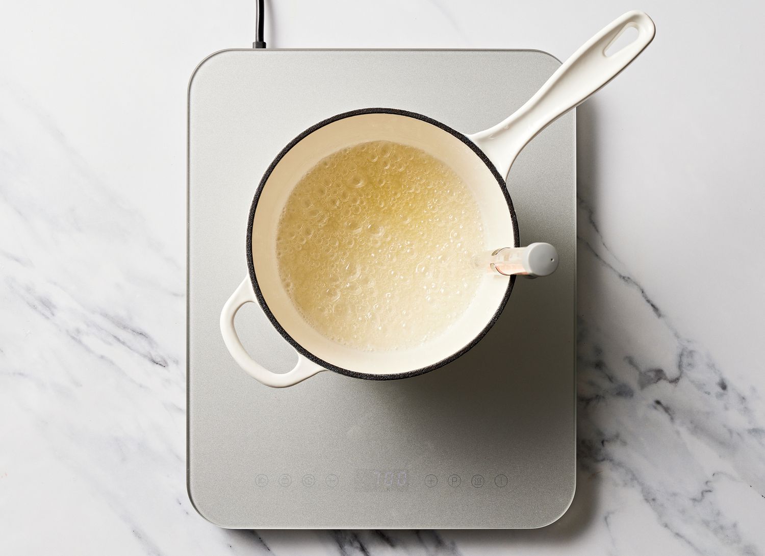 cooking white liquid with a candy thermometer in a pot