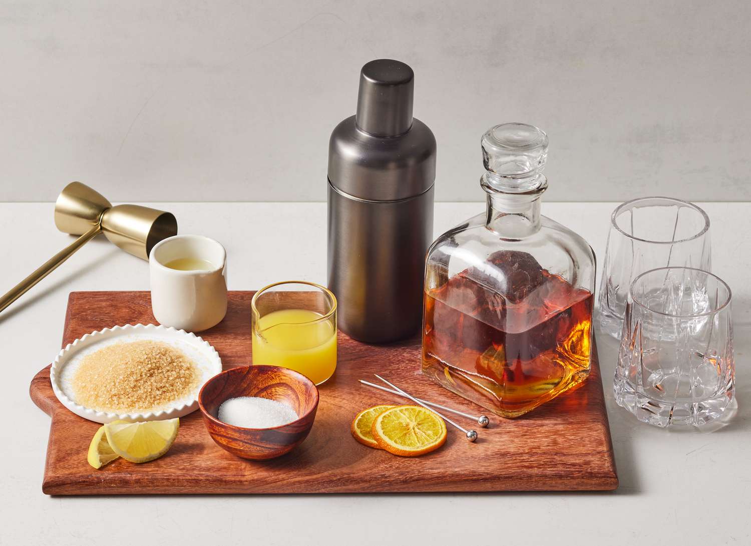 metal cocktail shaker, whiskey and cocktail ingredients on wooden cutting board