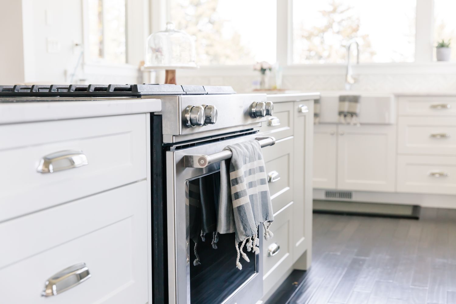 Modern kitchen interior featuring a stove with a towel hanging on its handle surrounded by white cabinets and a sink in the background