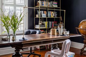 A study room featuring a wooden desk bookshelves stacked with books and a globe in the corner a chair positioned by the desk