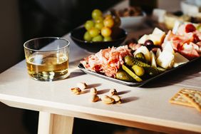 Charcuterie platter with meats cheeses crackers gherkins and a drink on a table
