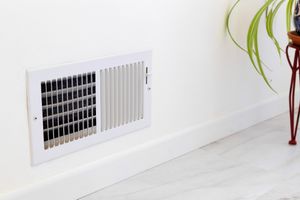 A wallmounted air vent with visible slats and a nearby green plant