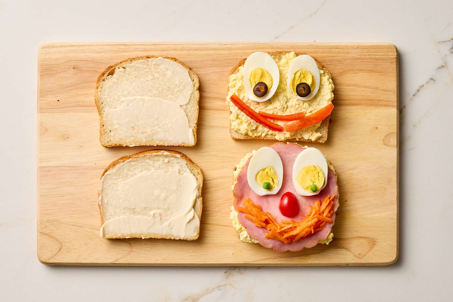 Two openfaced sandwiches decorated to resemble faces with ingredients like eggs olives and vegetables displayed on a wooden board