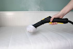 A handheld steam cleaner being used on a mattress