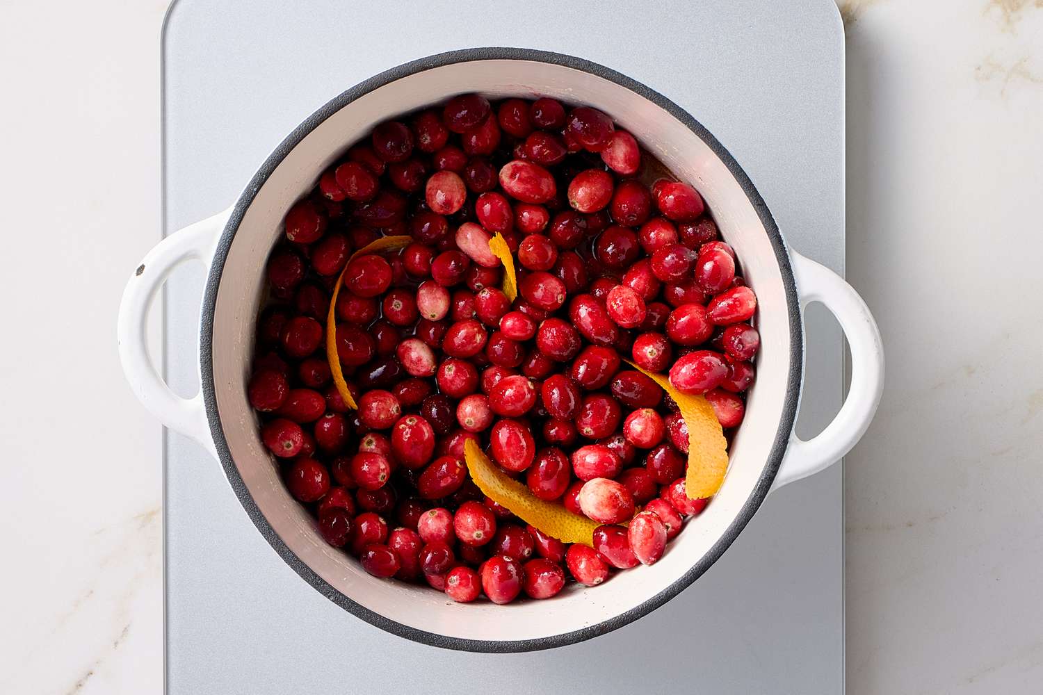 A pot containing fresh cranberries and orange peel