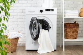 A washing machine with a towel partially out of the open door situated in a home laundry space with baskets nearby