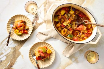 A serving dish and plates of ratatouille with glasses of wine
