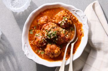 Plate of meatballs in tomato sauce with a spoon and fork garnished with cheese and herbs
