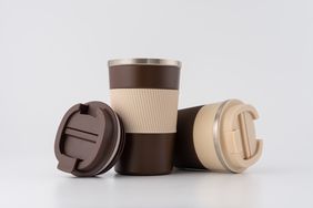 Three reusable coffee cups with lids two placed on their sides and one standing upright featuring a ribbed grip design