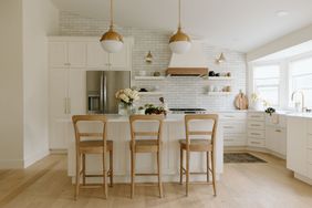 Modern kitchen with a central island and bar stools pendant lighting and white cabinets with stainless steel appliances