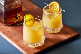 two whiskey sours and bottle of whiskey on wooden cutting board