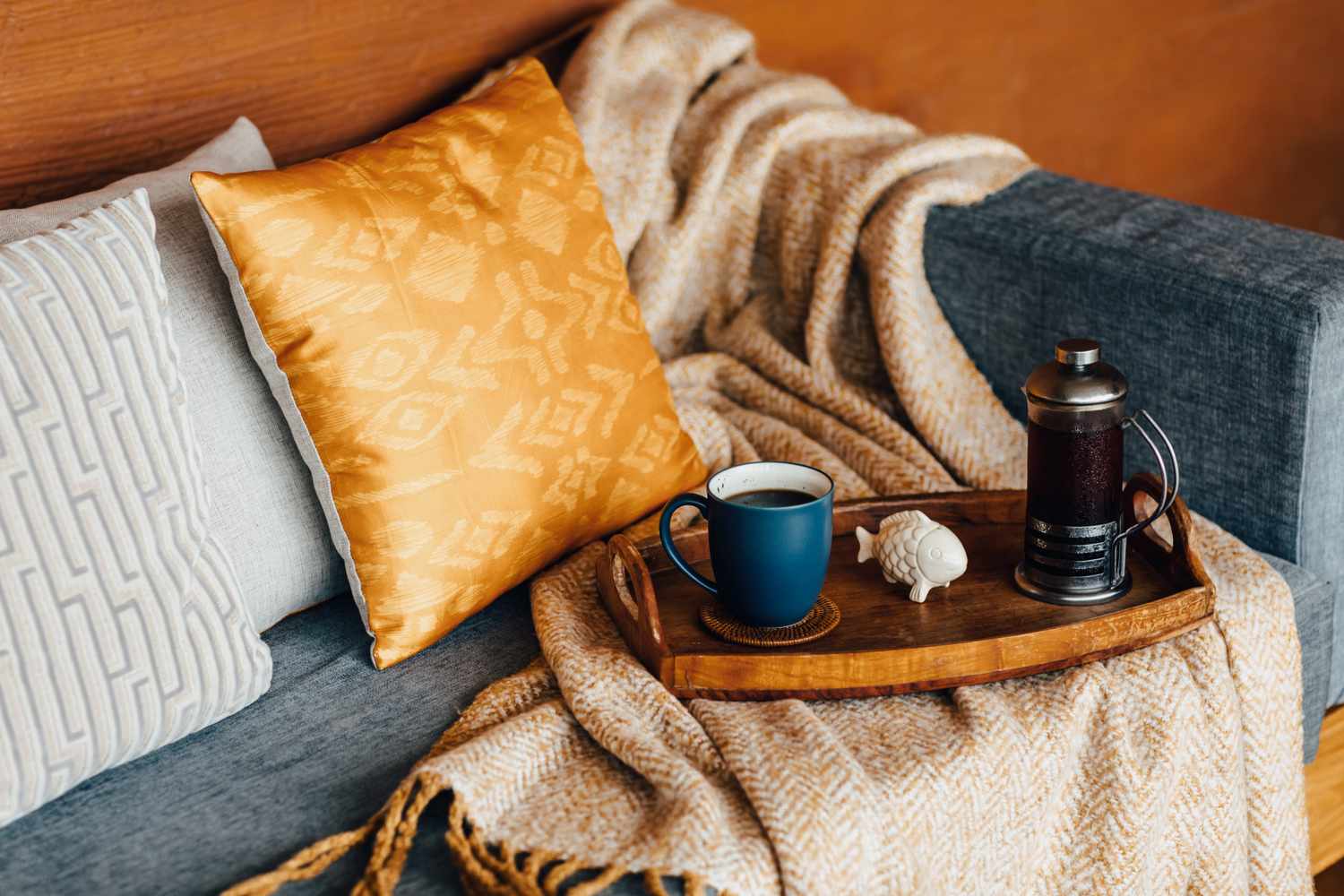 A cozy sofa with cushions and a blanket a wooden tray holding a coffee mug and a French press