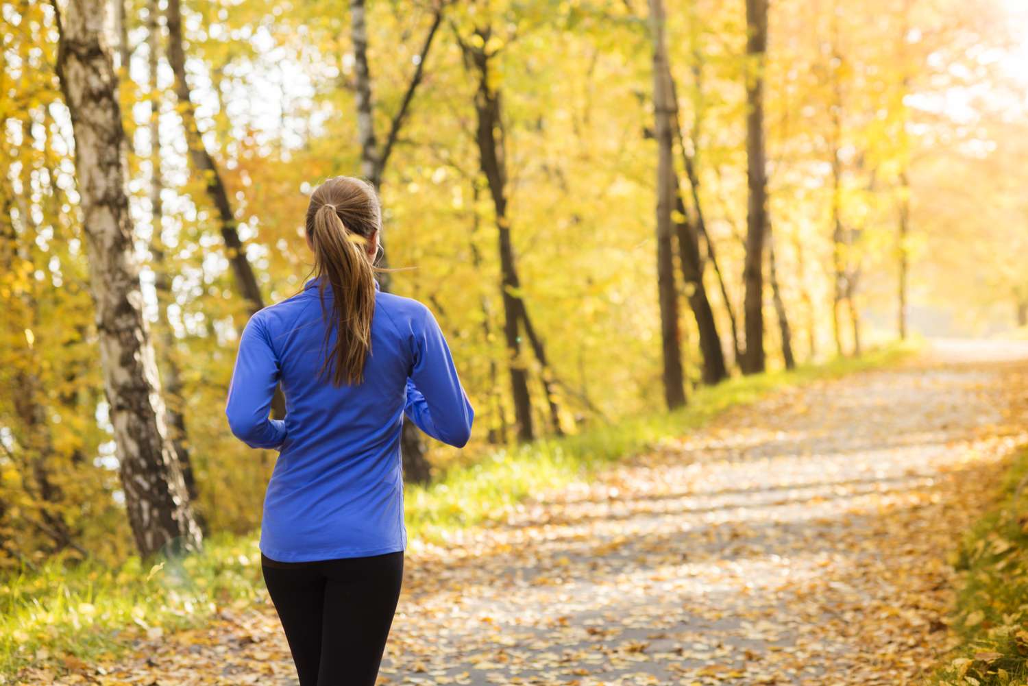 A person running on a forest path in an autumn setting with trees and fallen leaves around