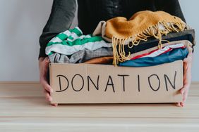 Woman holding cardboard donation box full with folded clothes