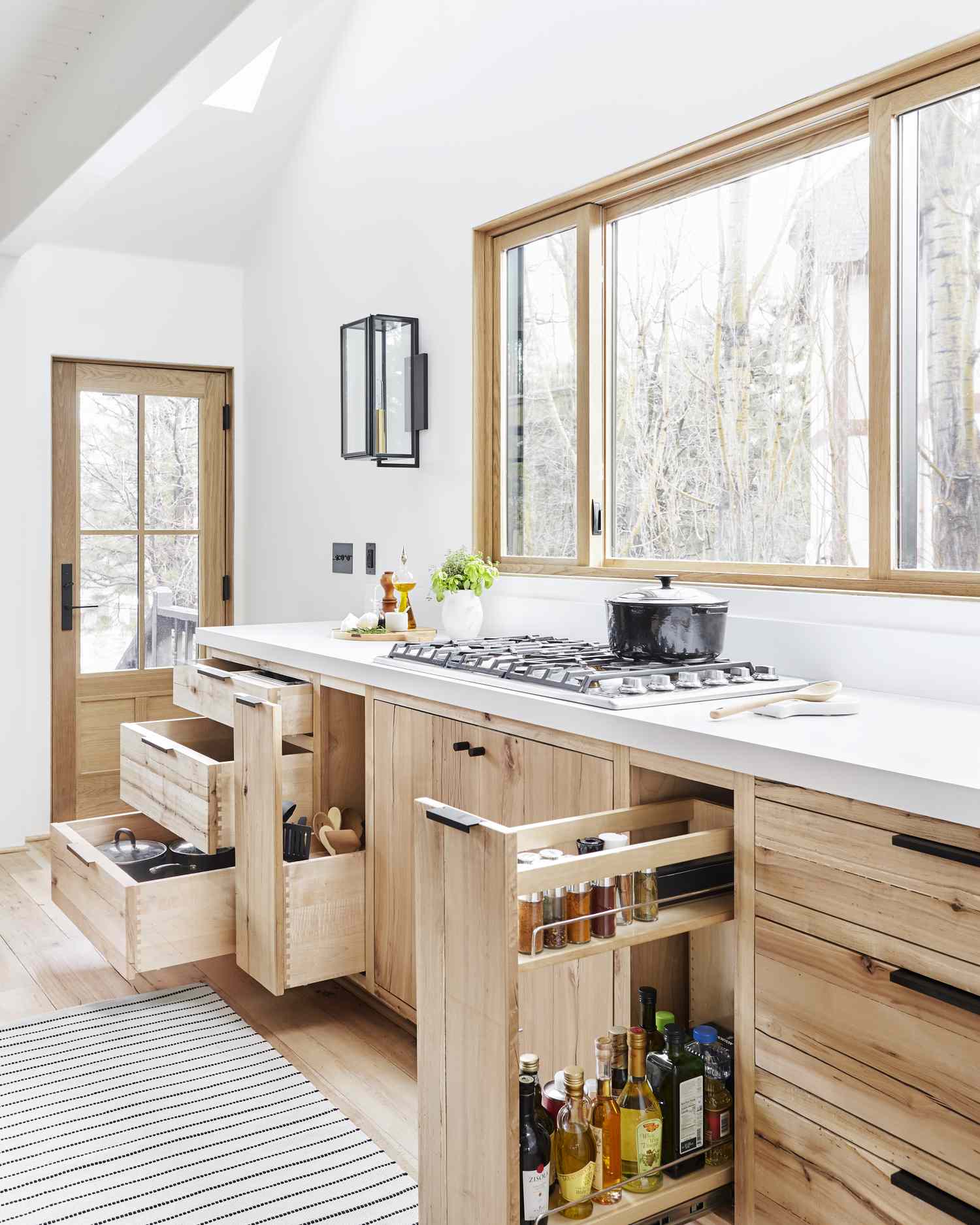 A modern kitchen with wooden cabinets open drawers revealing storage a stovetop large window and natural light