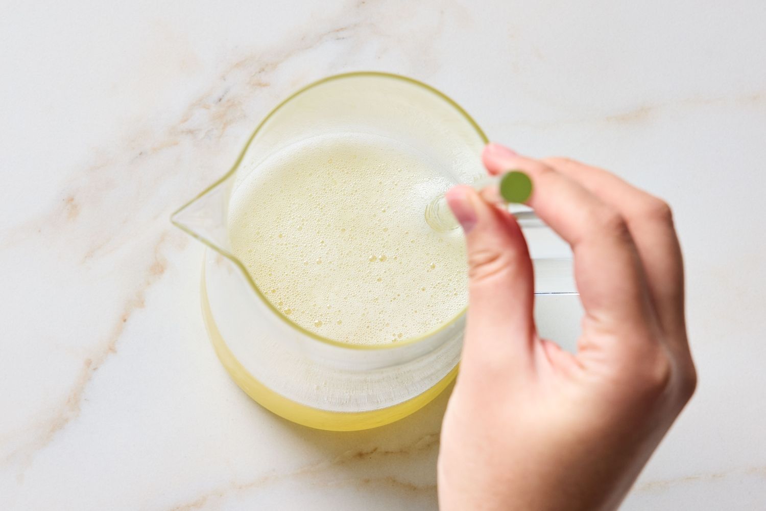 Hand holding a small ingredient above a pitcher with a liquid