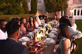 A group of people seated around a long table enjoying an outdoor dinner event in a garden setting