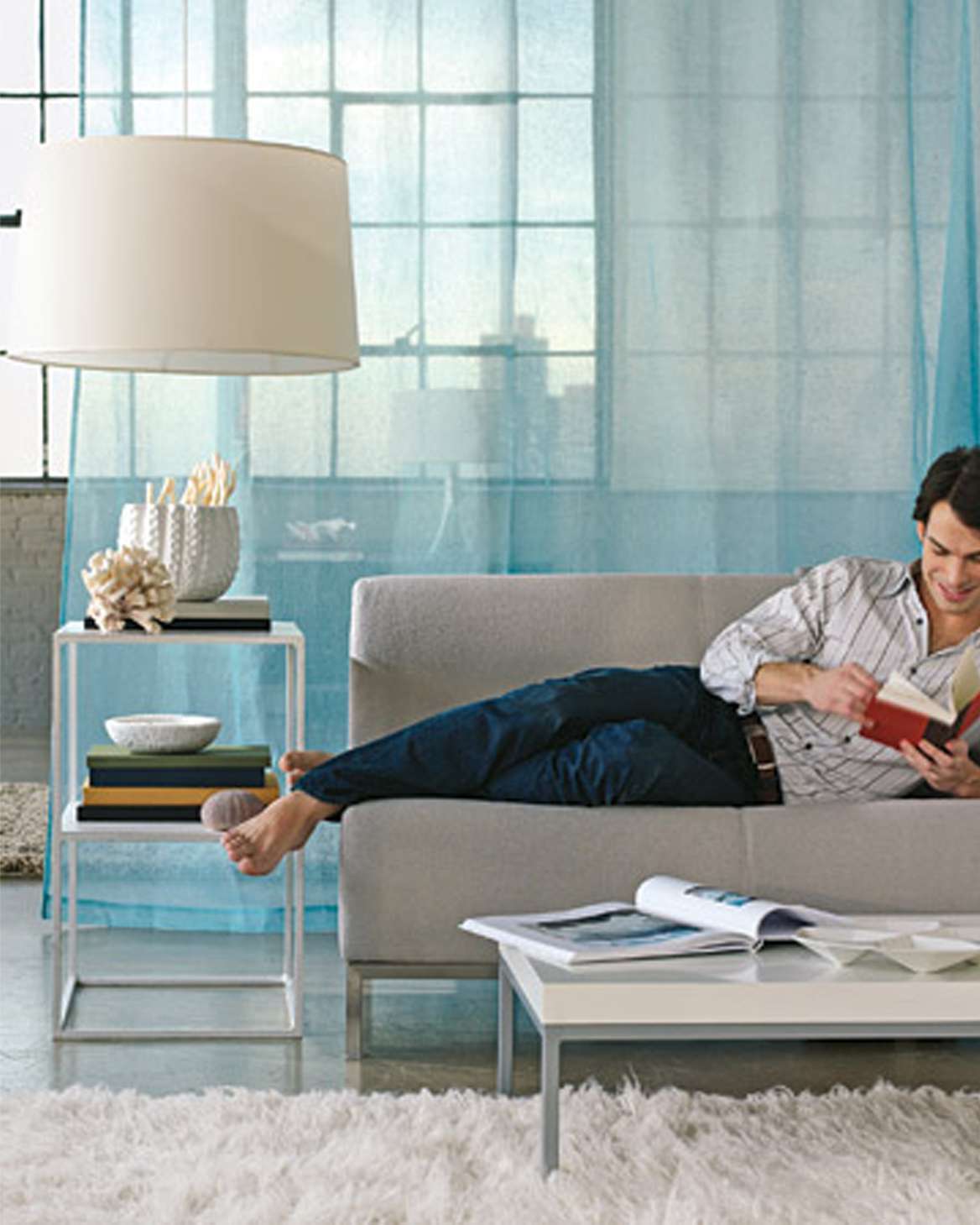 man laying on sofa reading with curtain room divider behind