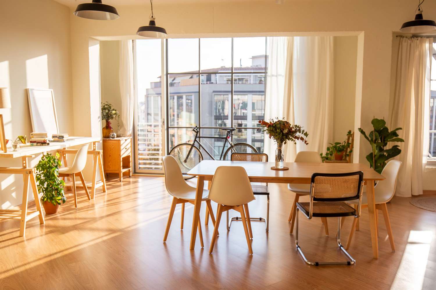 A bright and spacious modern dining area with a table chairs potted plants and large windows overlooking a building exterior