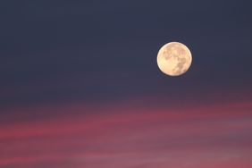 The full moon in the sky during twilight with a gradient of blue and red clouds
