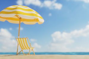 A beach chair and umbrella on a sandy beach with the ocean in the background