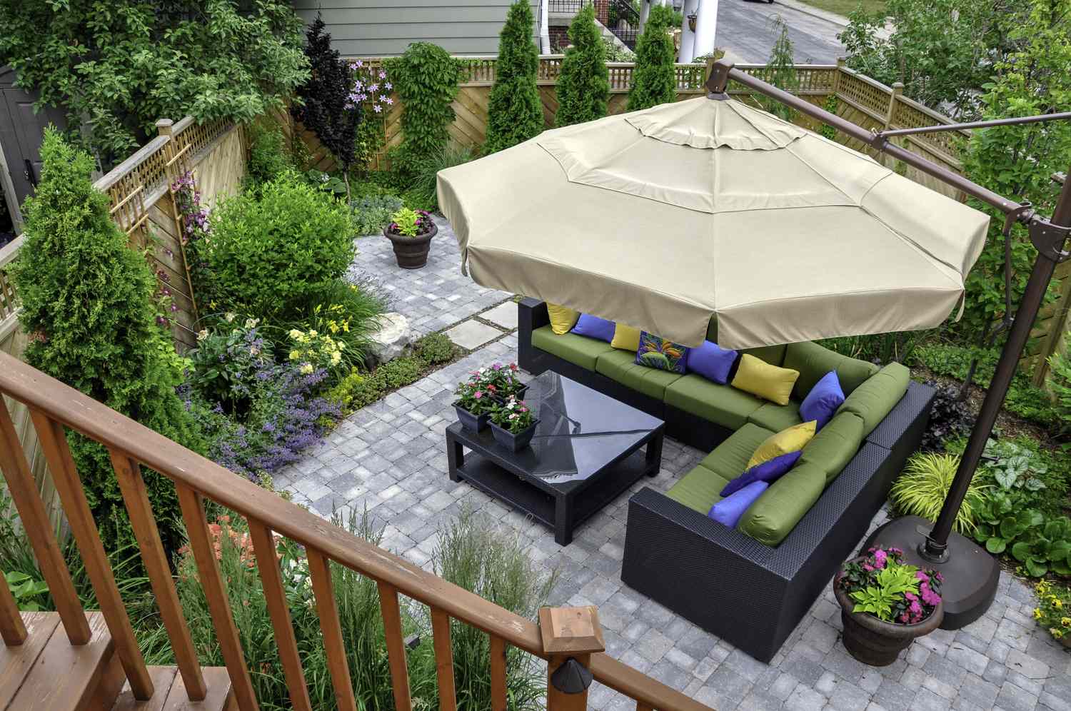 A backyard patio with seating area under a large umbrella surrounded by plants and a wooden fence