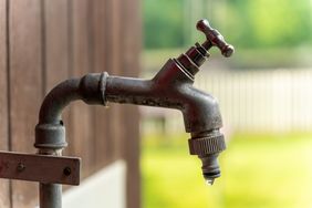 An outdoor faucet with a single drip of water hanging at its outlet