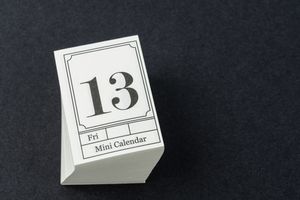 A mini desk calendar displaying the number 13 and the day Friday on a dark surface
