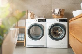 A washer and dryer set side by side in a laundry room with laundry items and a basket above them