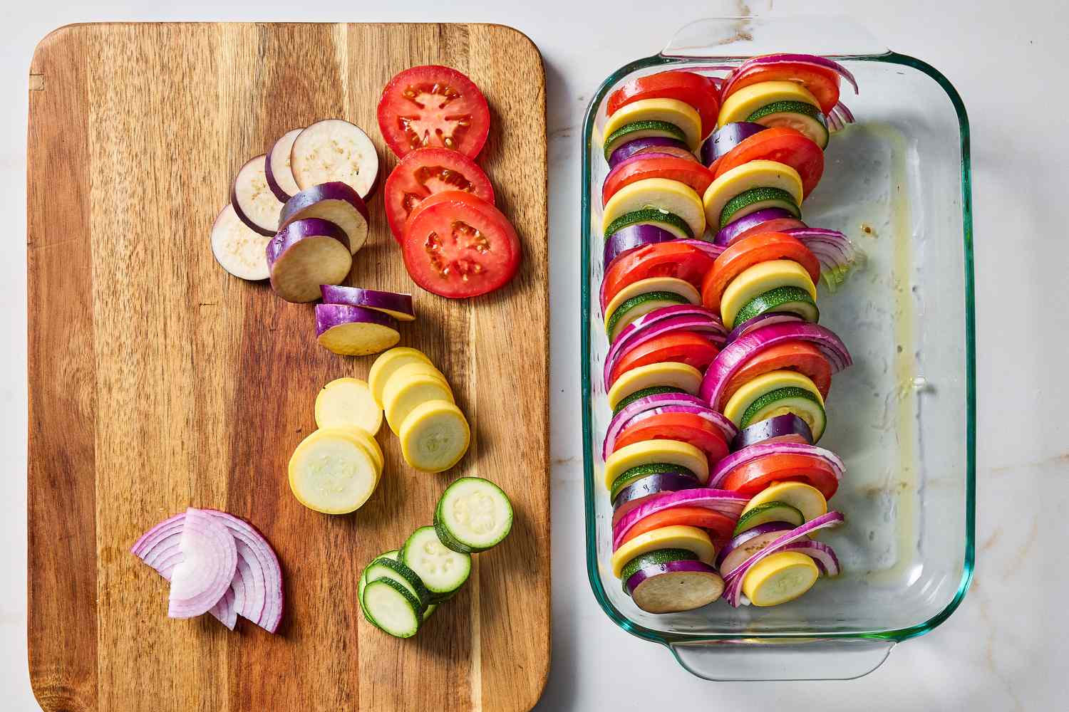 Sliced vegetables on a wooden board beside a tray of layered vegetable slices