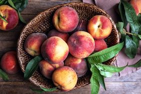 A basket filled with peaches and leaves on a wooden table