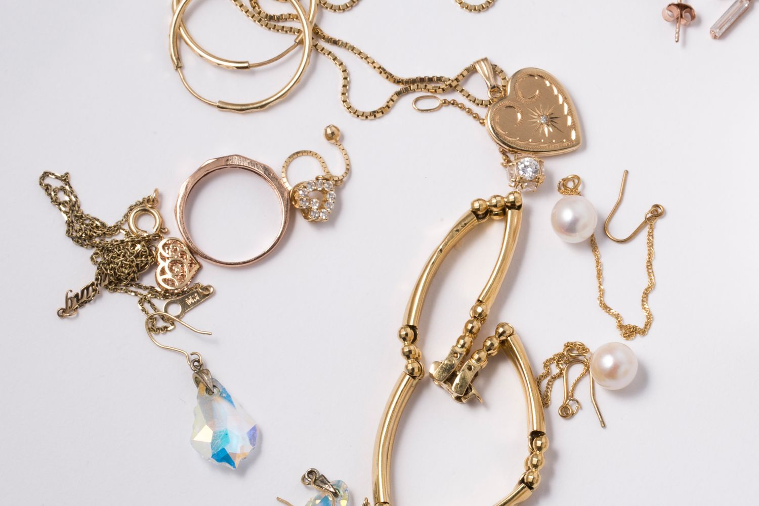 Assorted gold jewelry including chains bracelets rings pearl earrings and pendants on a flat surface