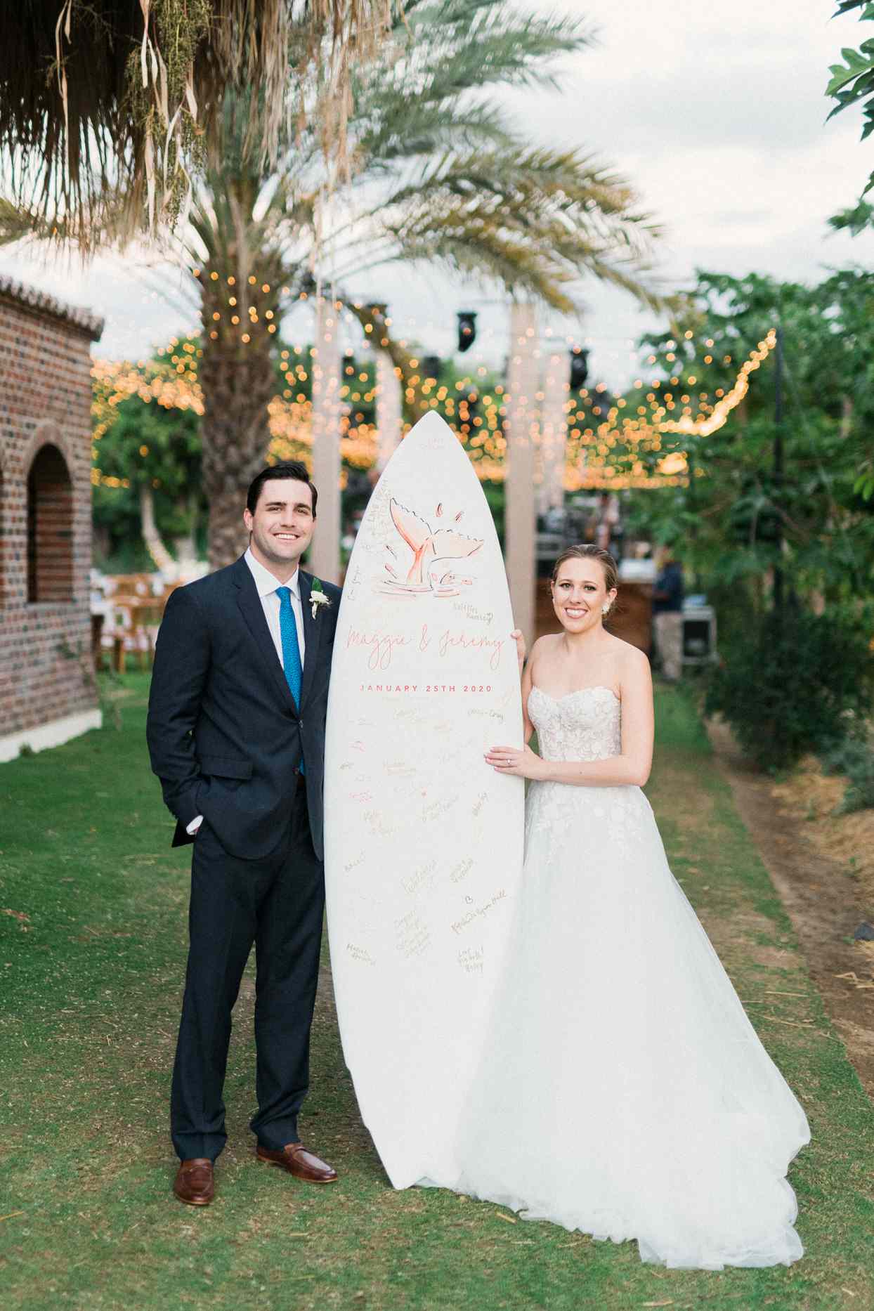 bride and groom posing with guest book surf board