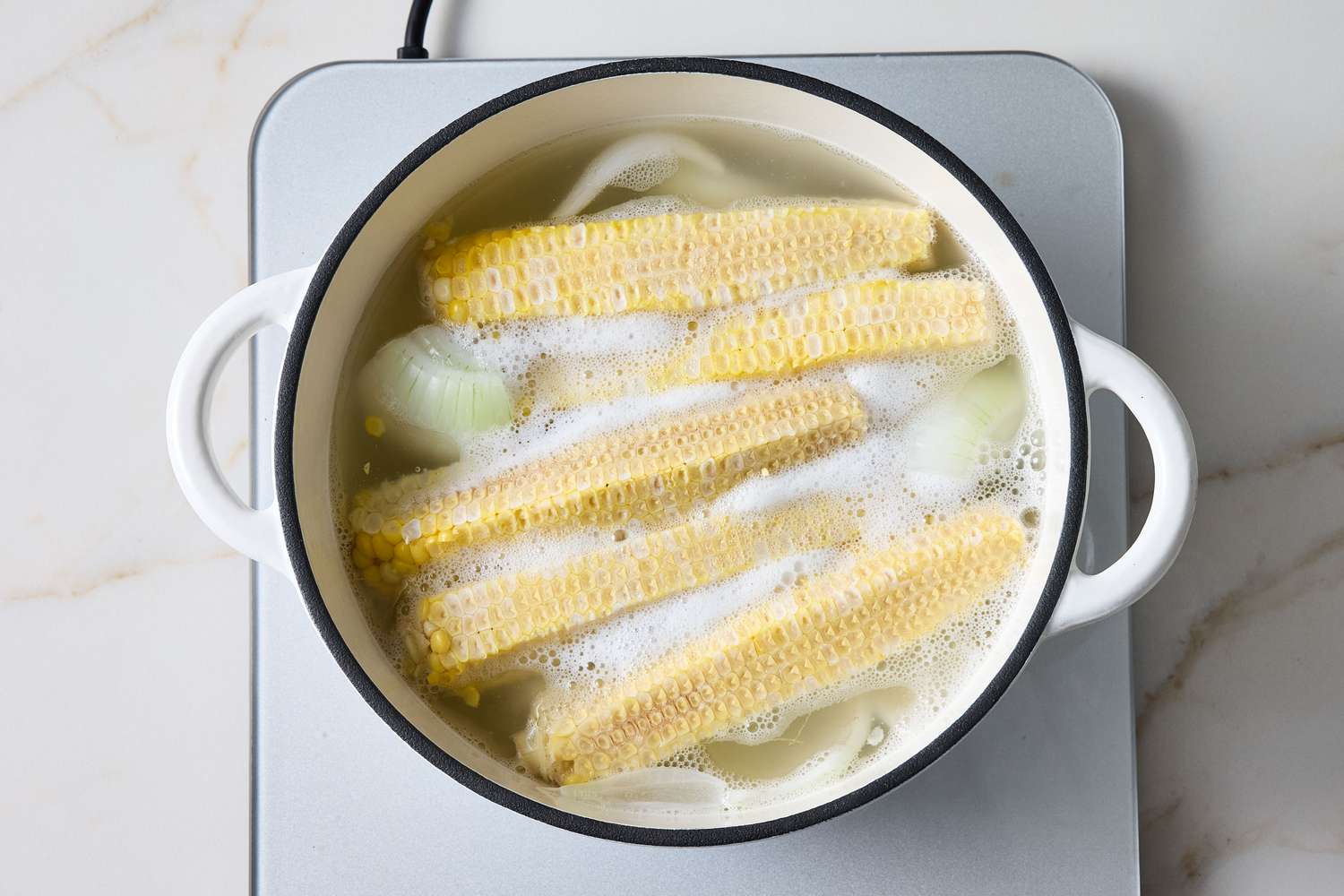 Corn on the cob boiling in a pot of water on a stovetop