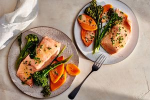 Two plates with salmon broccolini and slices of yam or carrot arranged as a meal photographed on a bright tabletop