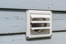 A closeup of an exterior wall dryer vent with a visible exhaust duct inside