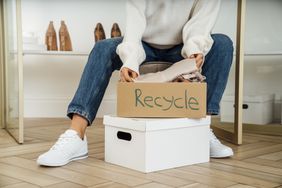 A person sits holding a box labeled Recycle containing items with another box placed below